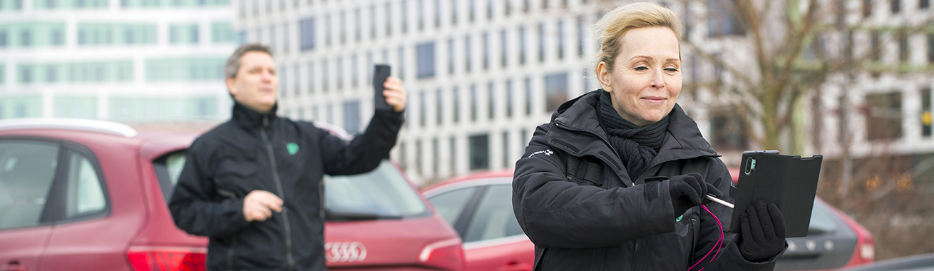 Två parkeringsvakter som håller upp sina mobiltelefoner för att läsa av bilarnas registreringsnummer