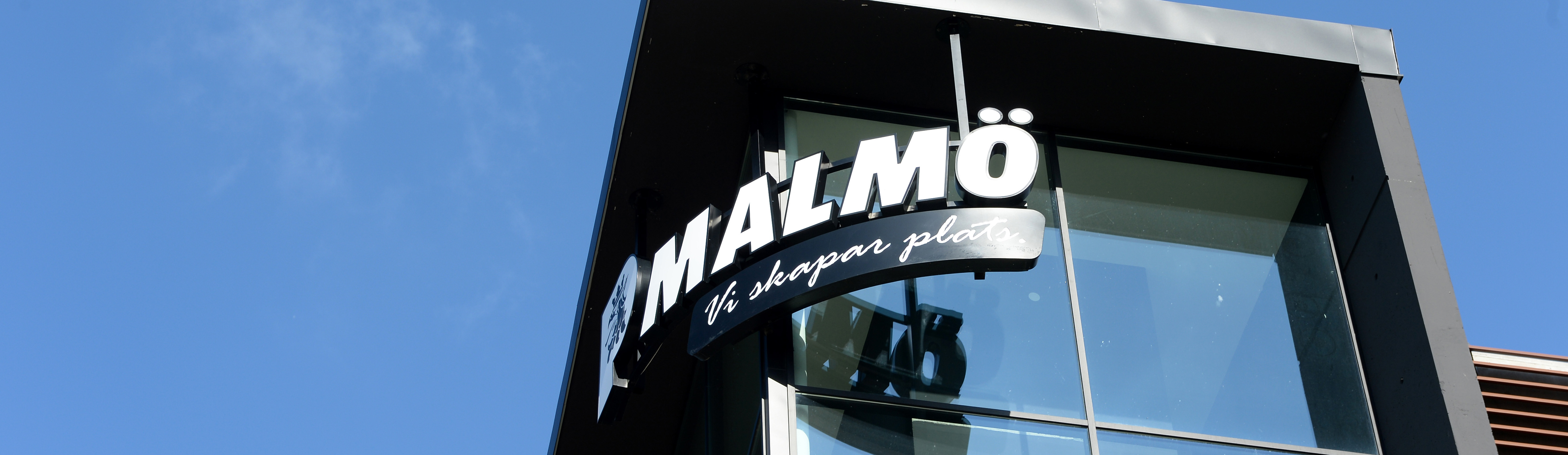 Parkerings Malmös logotype i vitt på P-huset Hyllie Allés fasad med en klarblå himmel i bakgrunden