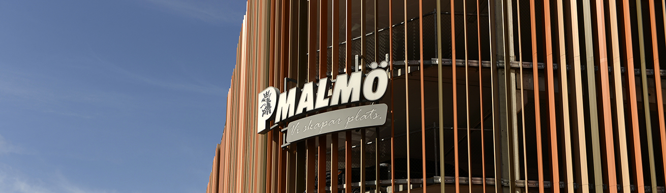 Parkering Malmös logotype i vitt på P-huset Godsmagasinet med en blå himmel i bakgrunden